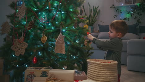 Kleiner-Junge-Schmückt-Am-Heiligabend-Den-Weihnachtsbaum-Und-Trägt-Eine-Glaskugel.-Hochwertiges-4K-Filmmaterial
